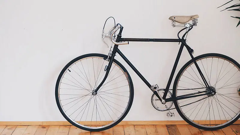 Black bicycle leaning against a white wall, wooden floor. 