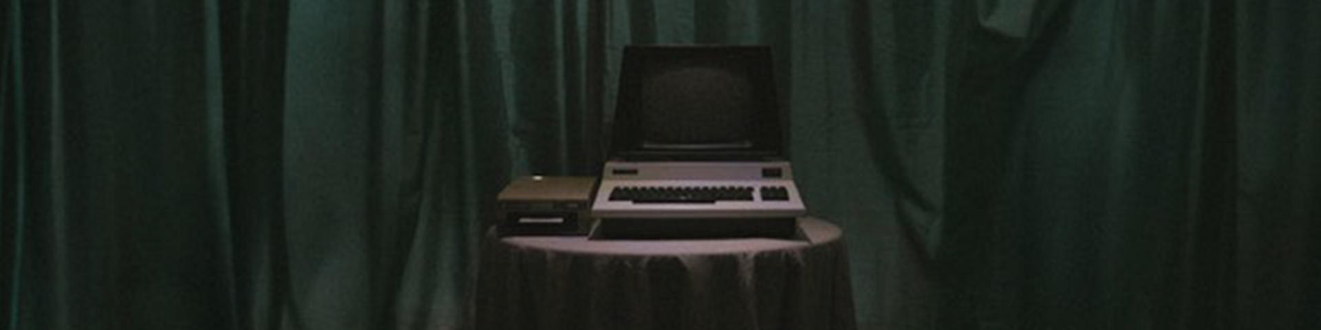 A computer on a table infront of a green curtain. Taken from the music vidoe