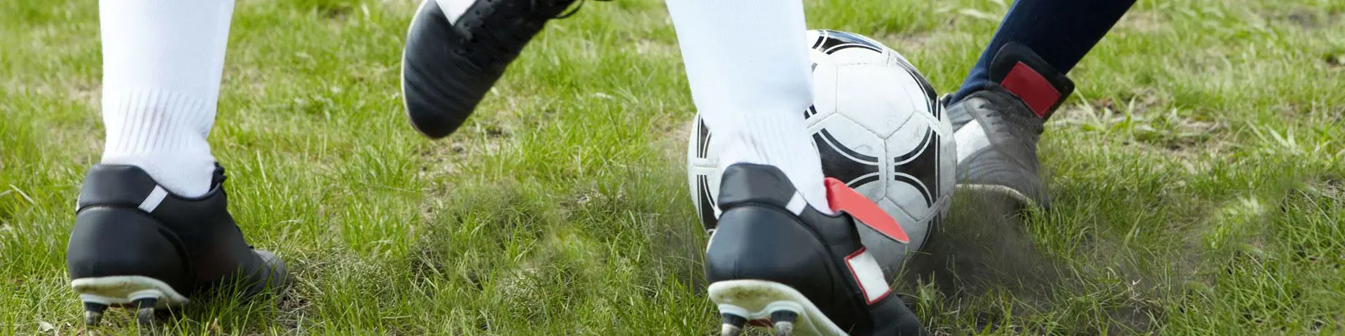 four feet in foot ball trainers kicking a football