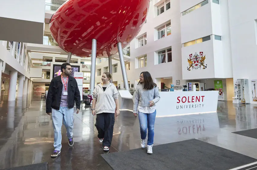 Three students walking through the Spark Atrium with the Pod in the background
