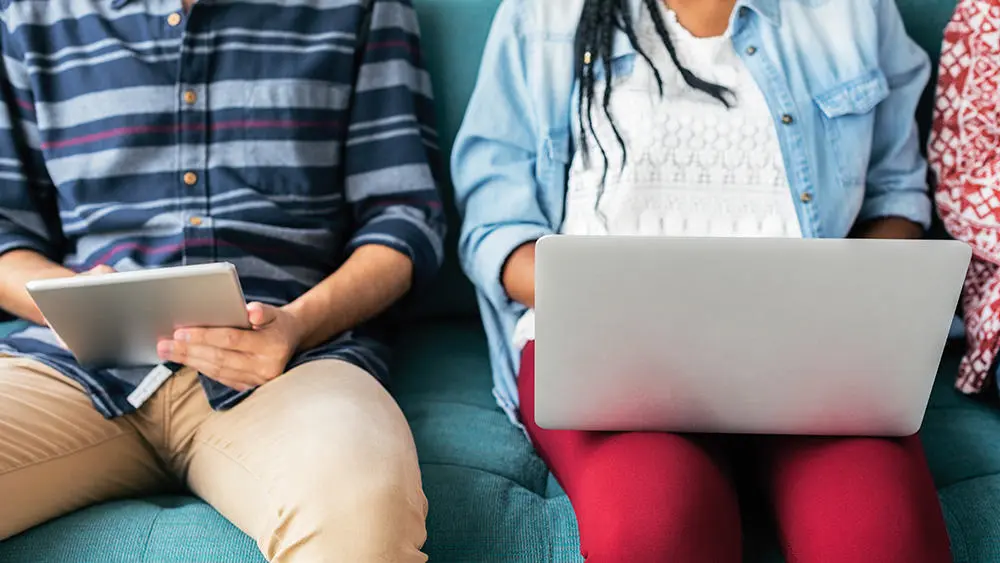 Two students sat on a bench on a laptop and ipad